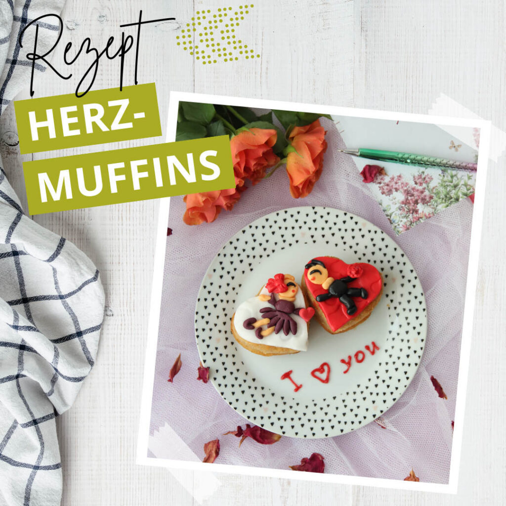 Ein Teller mit zwei herzförmig verzierten Muffins und der Aufschrift "I ♥ you" in Zuckerguss, umgeben von Blumen, einem Notizbuch und einem Küchentuch. Der Text "Rezept HERZ-MUFFINS" ist auf dem Bild zu sehen.