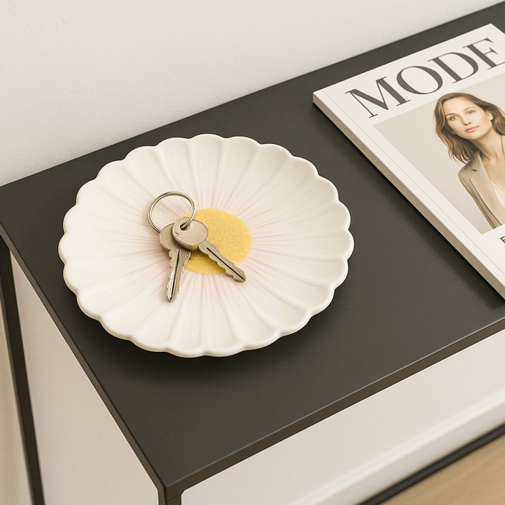 Eine weiße Gänseblümchenschale mit einem Schlüsselbund steht auf einem schwarzen Tisch neben einer Modezeitschrift mit einer Frau auf dem Cover.