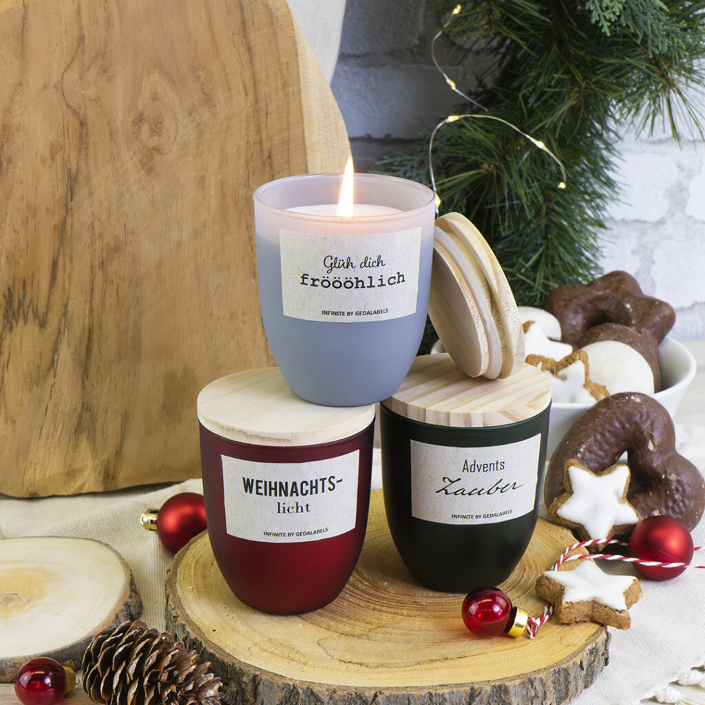 Drei festliche Kerzen mit Holzdeckeln stehen auf einem festlichen Tisch mit Weihnachtsgebäck, Tannenzapfen und Grünzeug. Eine Kerze ist angezündet und schafft eine warme und gemütliche Atmosphäre.