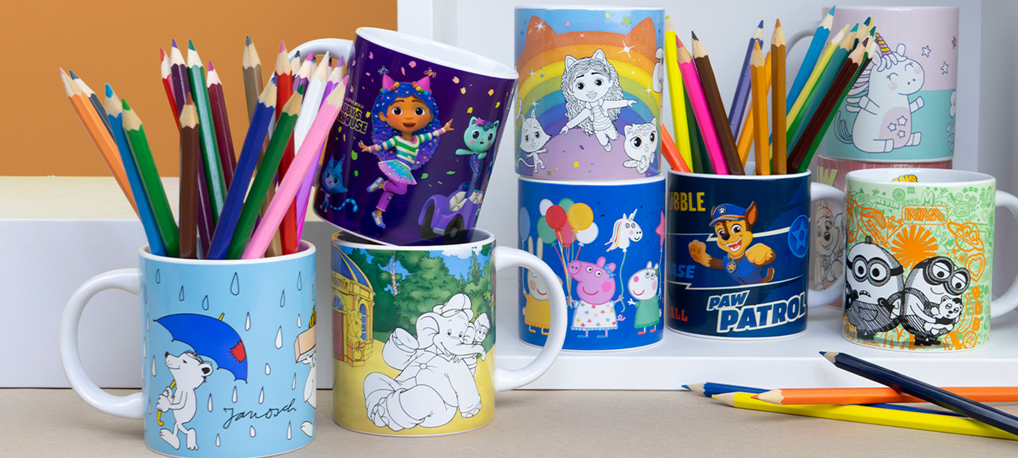 Bunte Tassen mit verschiedenen Cartoon-Figuren und Motiven dienen als Behälter für Buntstifte, die auf einem Schreibtisch mit zusätzlichen Buntstiften in der Nähe liegen.