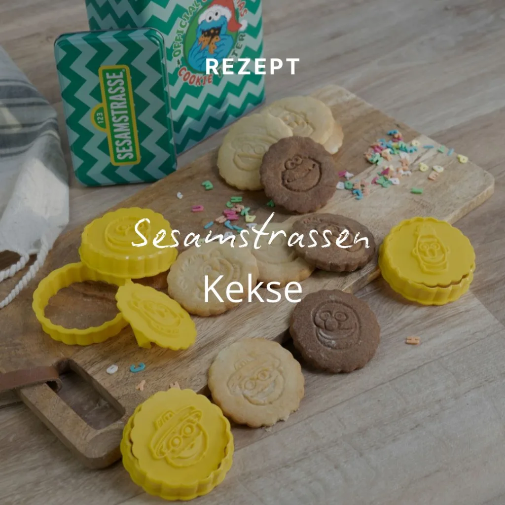 Ausstechformen mit Motiven aus der Sesamstraße und gebackene Kekse mit den Gesichtern der Figuren auf einem Holzbrett, im Hintergrund eine grüne Keksdose.
