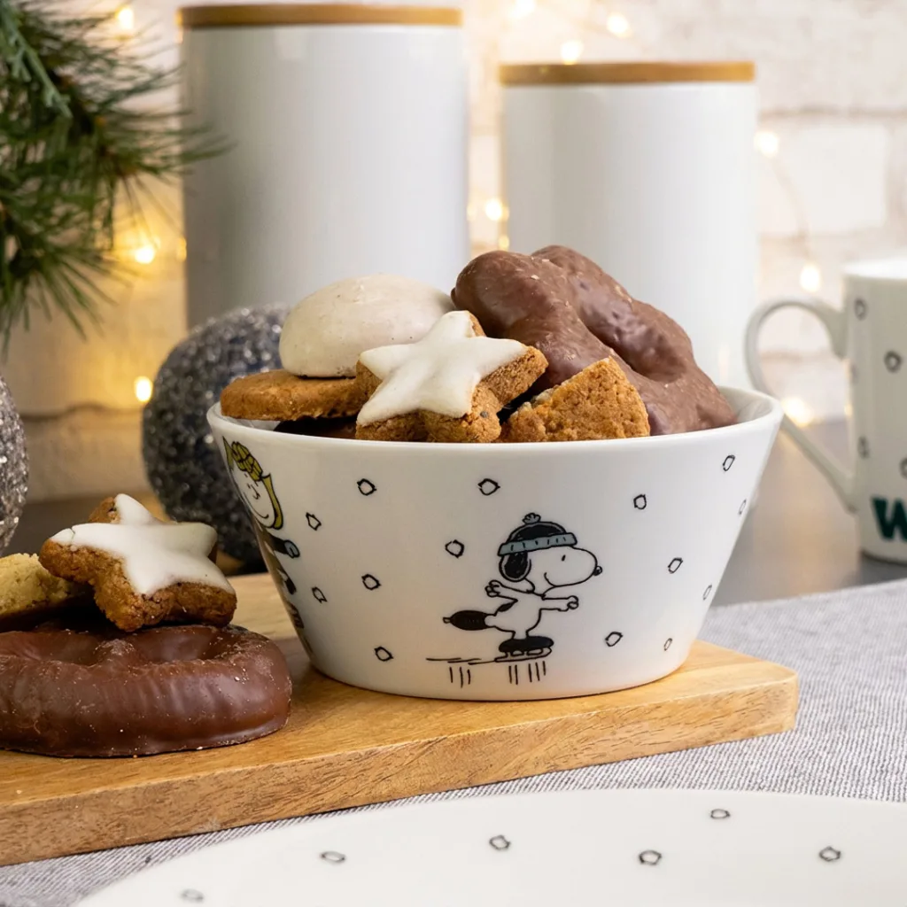 Eine Schale, verziert mit einer Abbildung von Snoopy beim Eislaufen, gefüllt mit verschiedenen schokoladenüberzogenen und sternförmigen Keksen.
