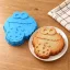 Eine blaue Silikon-Kuchenform in Form des Krümelmonsters neben einem gebackenen Kuchen im gleichen Design auf einem weißen Teller.