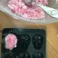 Eine durchsichtige Schale, gefüllt mit rosa-weißem Zuckerpeeling, neben einer silikonförmigen Form in Totenkopfform, deren eine Vertiefung mit der Mischung gefüllt ist.